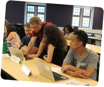 Instructor guiding a group of adults around a table with laptops